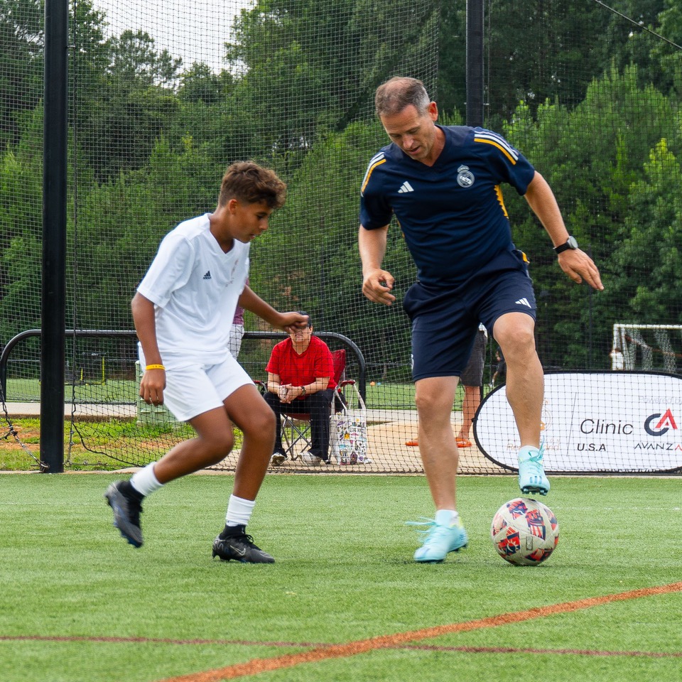 Jugando al futbol Entrenador y joven juegan fútbol en un campo al aire libre.